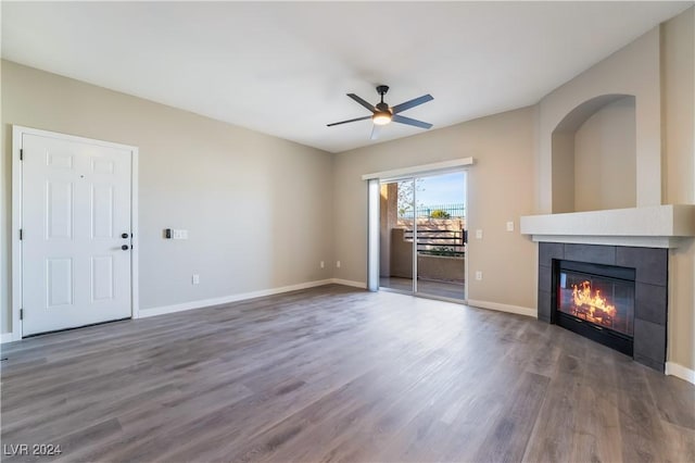 unfurnished living room featuring ceiling fan, dark wood-type flooring, and a tiled fireplace