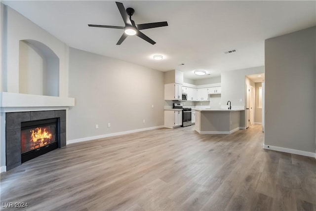 unfurnished living room with a tiled fireplace, ceiling fan, sink, and light hardwood / wood-style floors