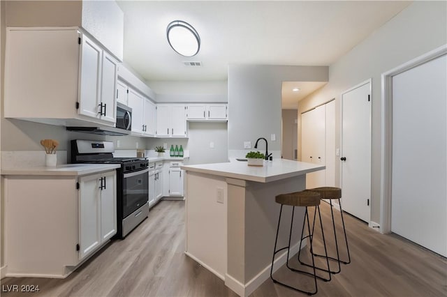 kitchen with a center island with sink, light hardwood / wood-style flooring, appliances with stainless steel finishes, a kitchen bar, and white cabinetry