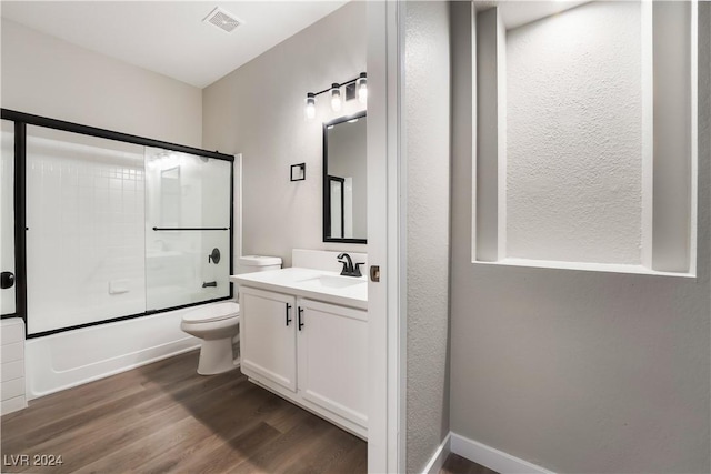 full bathroom featuring shower / bath combination with glass door, vanity, hardwood / wood-style flooring, and toilet