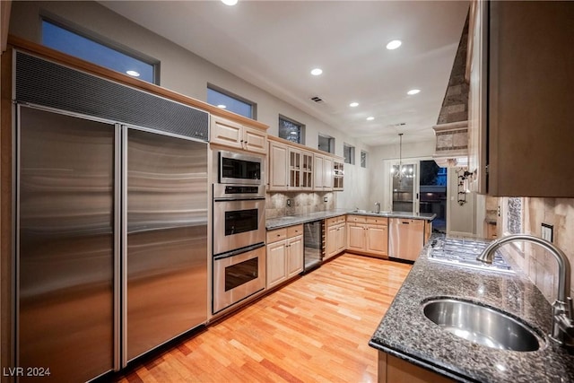 kitchen featuring beverage cooler, sink, built in appliances, decorative light fixtures, and light hardwood / wood-style flooring