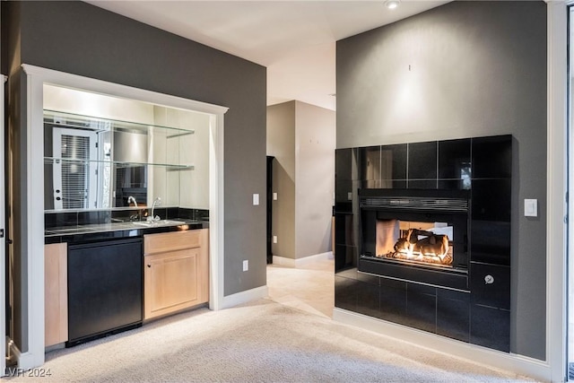 kitchen featuring a tile fireplace, light brown cabinets, sink, black dishwasher, and light colored carpet