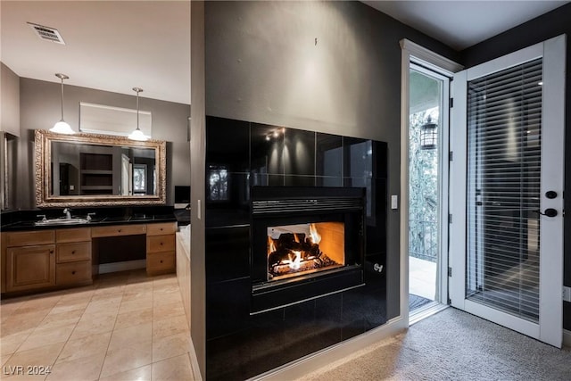 kitchen featuring a tile fireplace, sink, built in desk, decorative light fixtures, and light tile patterned flooring