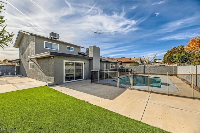 rear view of house with a fenced in pool, a lawn, cooling unit, and a patio