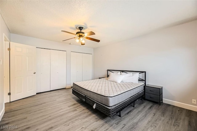 bedroom featuring a textured ceiling, ceiling fan, two closets, and light wood-type flooring