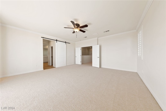 unfurnished bedroom with ceiling fan, a barn door, ornamental molding, and light carpet