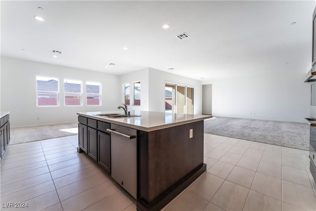 kitchen featuring dark brown cabinetry, a wealth of natural light, stainless steel dishwasher, light colored carpet, and a kitchen island with sink