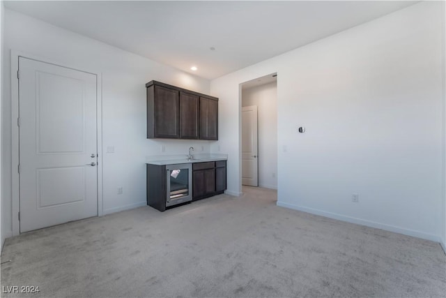 interior space featuring dark brown cabinets, light colored carpet, beverage cooler, and sink