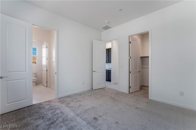 unfurnished bedroom featuring ensuite bathroom, a walk in closet, light carpet, and a closet