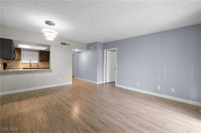 unfurnished living room featuring sink, a textured ceiling, and light hardwood / wood-style flooring