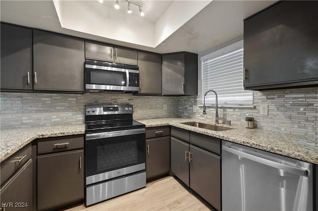 kitchen featuring sink, tasteful backsplash, light hardwood / wood-style flooring, stainless steel appliances, and light stone countertops