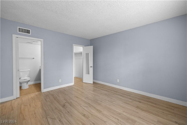 unfurnished bedroom featuring a walk in closet, a textured ceiling, light hardwood / wood-style floors, and ensuite bath