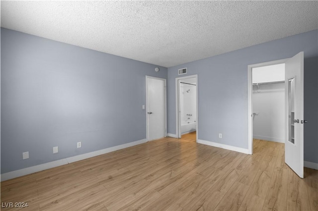 unfurnished bedroom featuring ensuite bath, light hardwood / wood-style floors, a textured ceiling, a walk in closet, and a closet