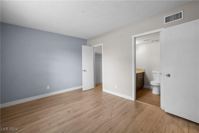 unfurnished bedroom with ensuite bath, a spacious closet, light hardwood / wood-style flooring, a textured ceiling, and a closet