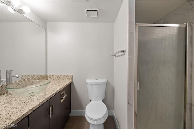 bathroom with a shower with door, vanity, tile patterned flooring, and toilet