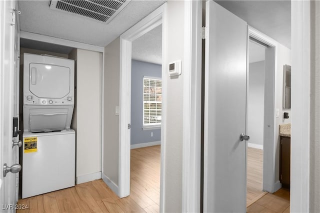 laundry room with stacked washer / drying machine, a textured ceiling, and light wood-type flooring