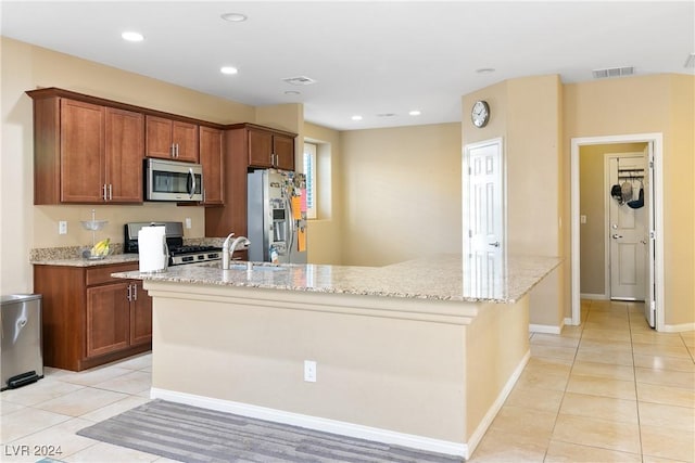 kitchen with appliances with stainless steel finishes, light stone counters, a kitchen island with sink, sink, and light tile patterned floors