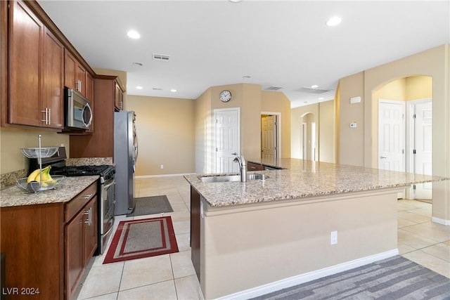 kitchen with light stone countertops, sink, an island with sink, light tile patterned floors, and appliances with stainless steel finishes