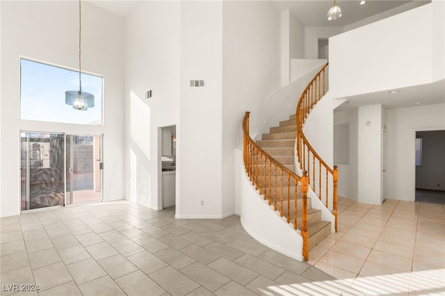 stairway with a towering ceiling, tile patterned flooring, and a chandelier