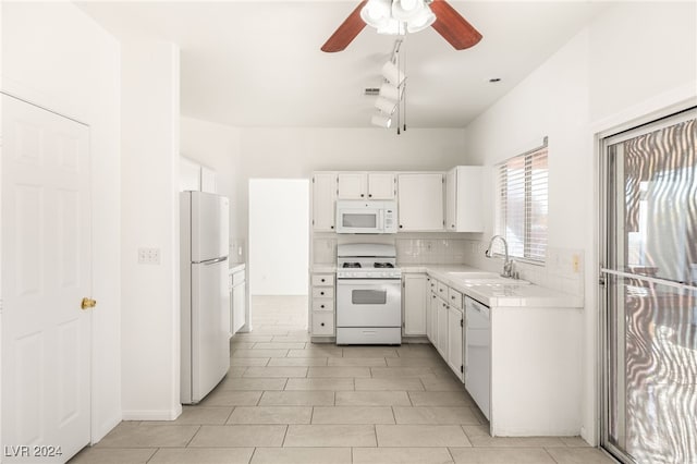 kitchen with white appliances, tasteful backsplash, rail lighting, white cabinets, and sink