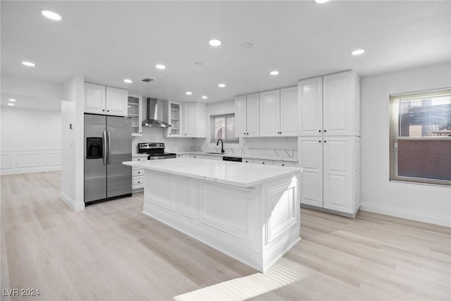 kitchen featuring wall chimney exhaust hood, a kitchen island, white cabinetry, appliances with stainless steel finishes, and sink