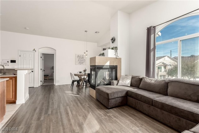 living room with a multi sided fireplace, light hardwood / wood-style floors, lofted ceiling, and sink