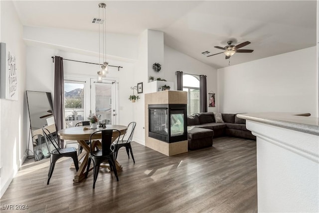 dining space with a tiled fireplace, plenty of natural light, dark wood-type flooring, and vaulted ceiling