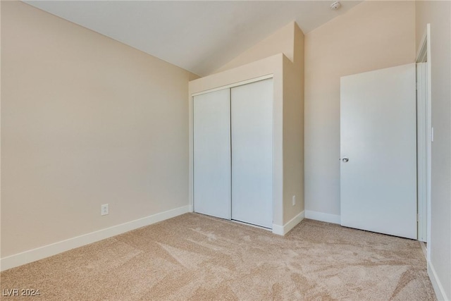 unfurnished bedroom featuring light carpet, vaulted ceiling, and a closet