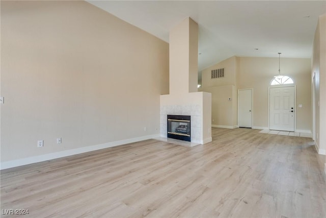 unfurnished living room with a tiled fireplace, high vaulted ceiling, and light wood-type flooring