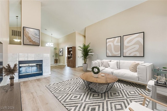 living room with a tiled fireplace, high vaulted ceiling, and light hardwood / wood-style floors