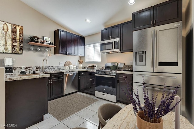 kitchen with light tile patterned floors, sink, appliances with stainless steel finishes, light stone countertops, and vaulted ceiling