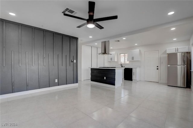 kitchen featuring stainless steel refrigerator, white cabinetry, ceiling fan, wall chimney exhaust hood, and a kitchen island