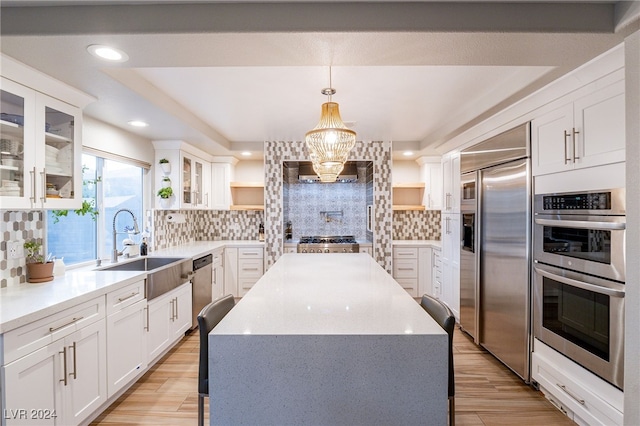 kitchen with decorative backsplash, hanging light fixtures, stainless steel appliances, and light hardwood / wood-style floors