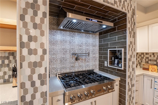 kitchen with tasteful backsplash, wall chimney exhaust hood, white cabinets, and stainless steel gas stovetop