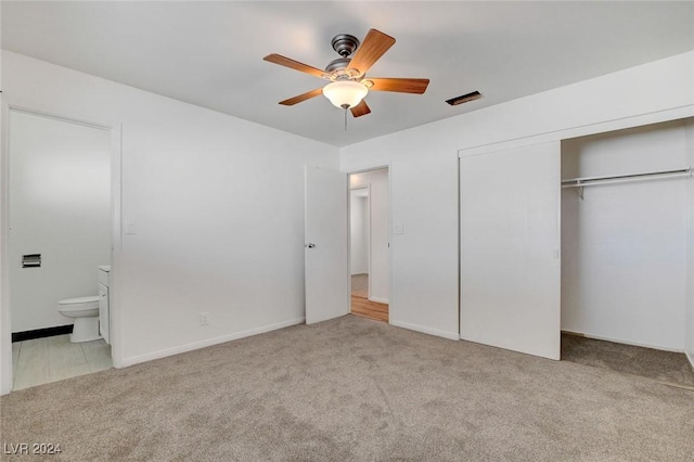 unfurnished bedroom featuring ceiling fan, light colored carpet, ensuite bathroom, and a closet