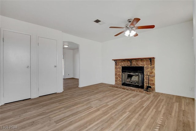 unfurnished living room featuring a stone fireplace, light hardwood / wood-style flooring, and ceiling fan