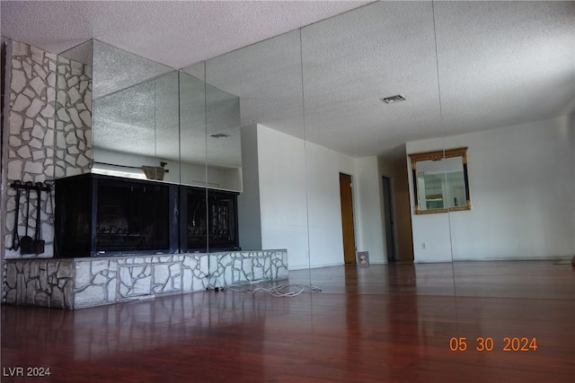 unfurnished living room featuring hardwood / wood-style floors, a stone fireplace, and a textured ceiling