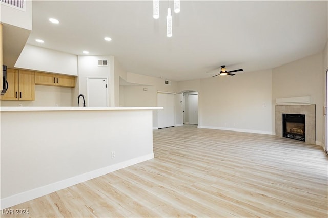 unfurnished living room featuring ceiling fan, light wood-type flooring, sink, and a tiled fireplace