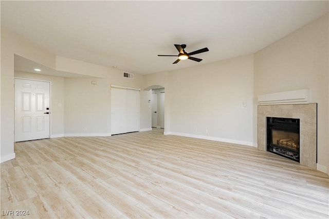 unfurnished living room with a wall unit AC, a tile fireplace, ceiling fan, and light wood-type flooring