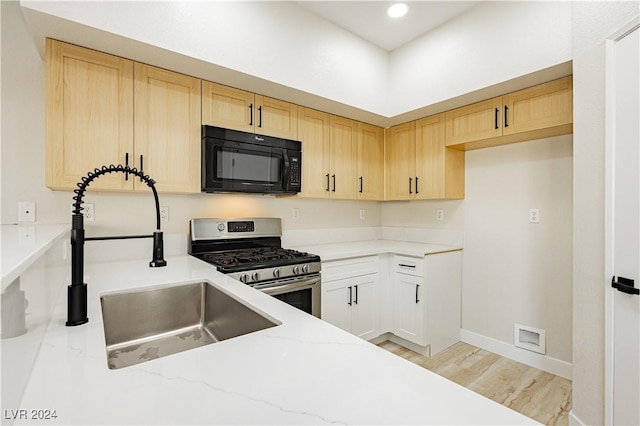 kitchen featuring stainless steel gas stove, sink, light stone counters, light brown cabinetry, and light wood-type flooring