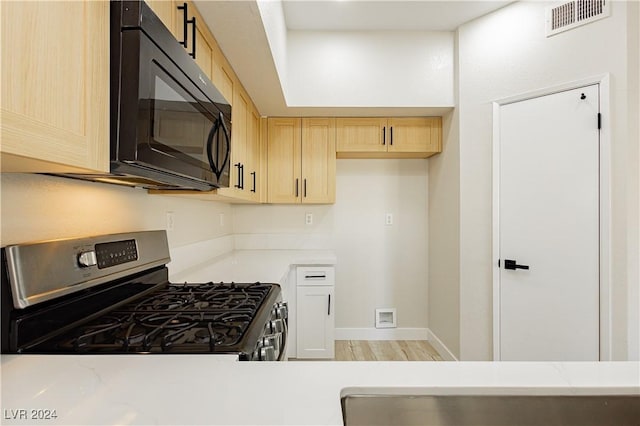 kitchen featuring light wood-type flooring, light brown cabinetry, stainless steel gas stove, and light stone countertops