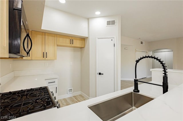 kitchen with gas stove, sink, light brown cabinetry, and light hardwood / wood-style flooring