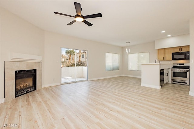 unfurnished living room with ceiling fan, a fireplace, and light wood-type flooring