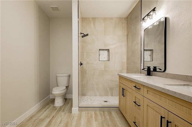 bathroom featuring toilet, wood-type flooring, vanity, and a tile shower