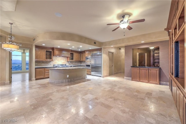 kitchen with built in appliances, decorative light fixtures, a center island, custom range hood, and ceiling fan with notable chandelier