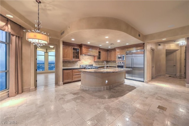 kitchen with a kitchen island with sink, a chandelier, hanging light fixtures, a water view, and built in appliances