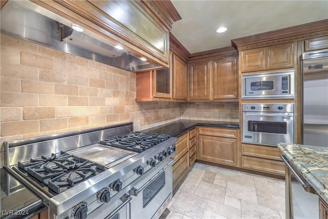 kitchen with dark stone counters, built in appliances, tasteful backsplash, and custom range hood