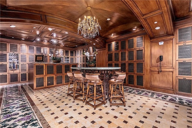 wine area with wooden walls, an inviting chandelier, indoor bar, lofted ceiling, and brick ceiling