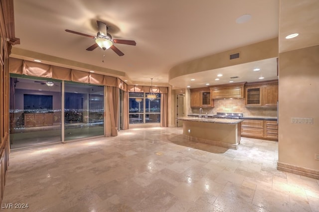 kitchen featuring ceiling fan, backsplash, premium range hood, a center island with sink, and pendant lighting