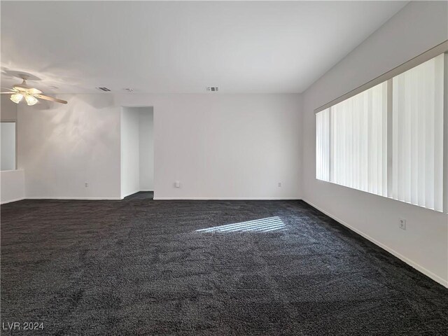 empty room with ceiling fan and dark colored carpet